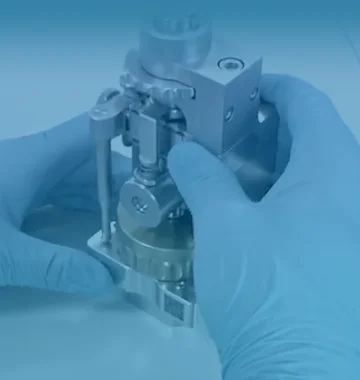 Close-up of gloved hands assembling a precision lab valve on a metal block in a lab setting.